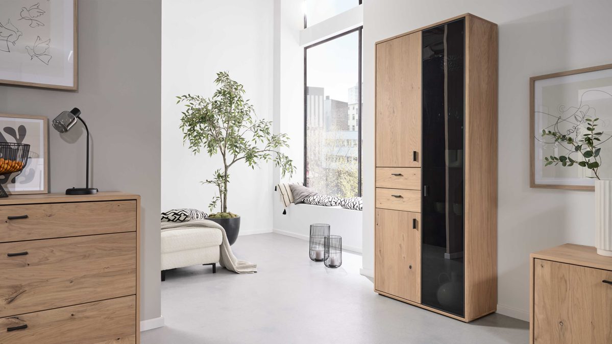 Vitrine Interliving aus Holz in Holzfarben Interliving Wohnzimmer Serie 2024 - Vitrine Eiche & Schwarzglas - drei Türen, zwei Schubladen, Breite ca. 85 cm