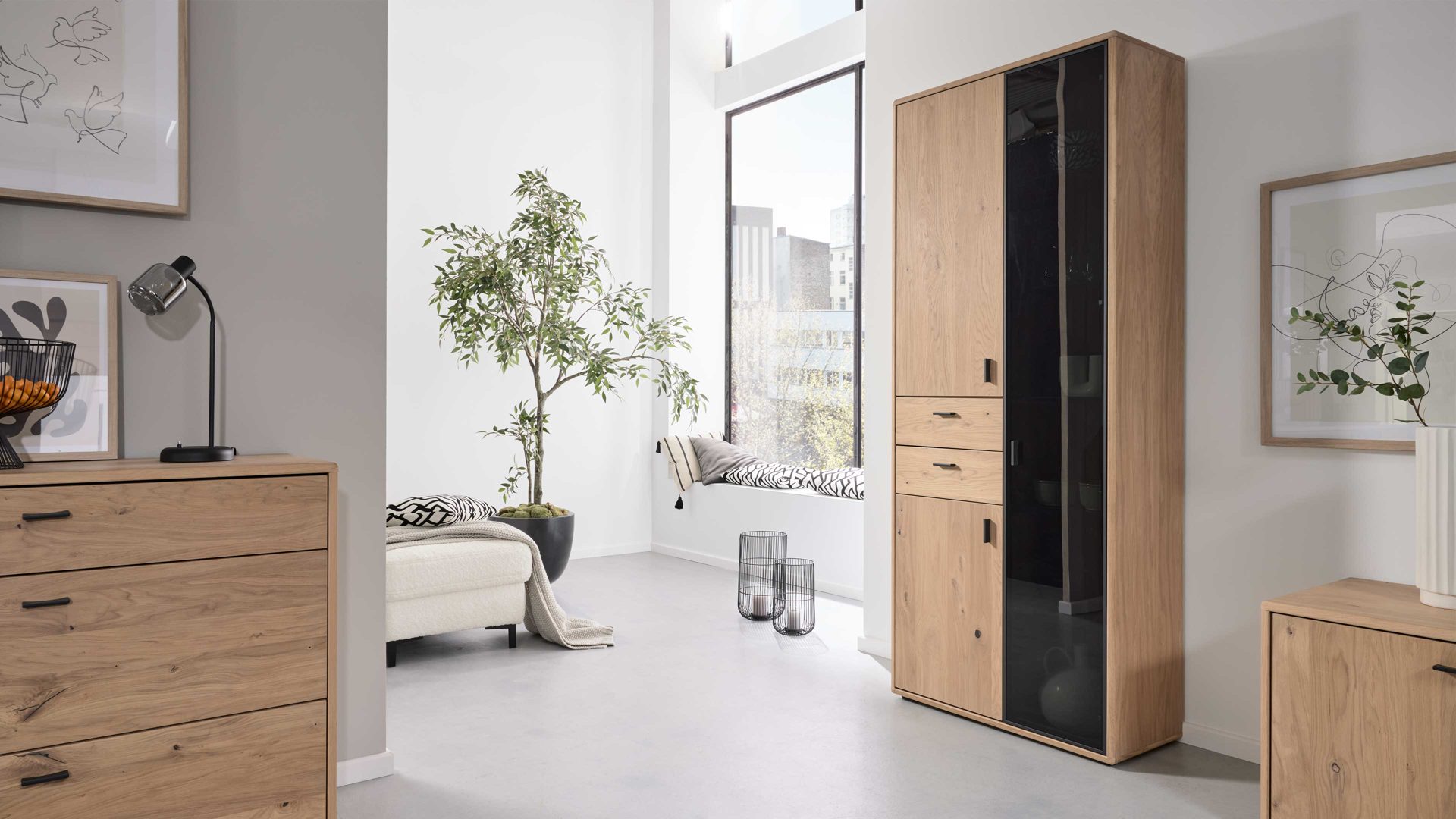 Vitrine Interliving aus Holz in Holzfarben Interliving Wohnzimmer Serie 2024 - Vitrine Eiche & Schwarzglas - drei Türen, zwei Schubladen, Breite ca. 85 cm