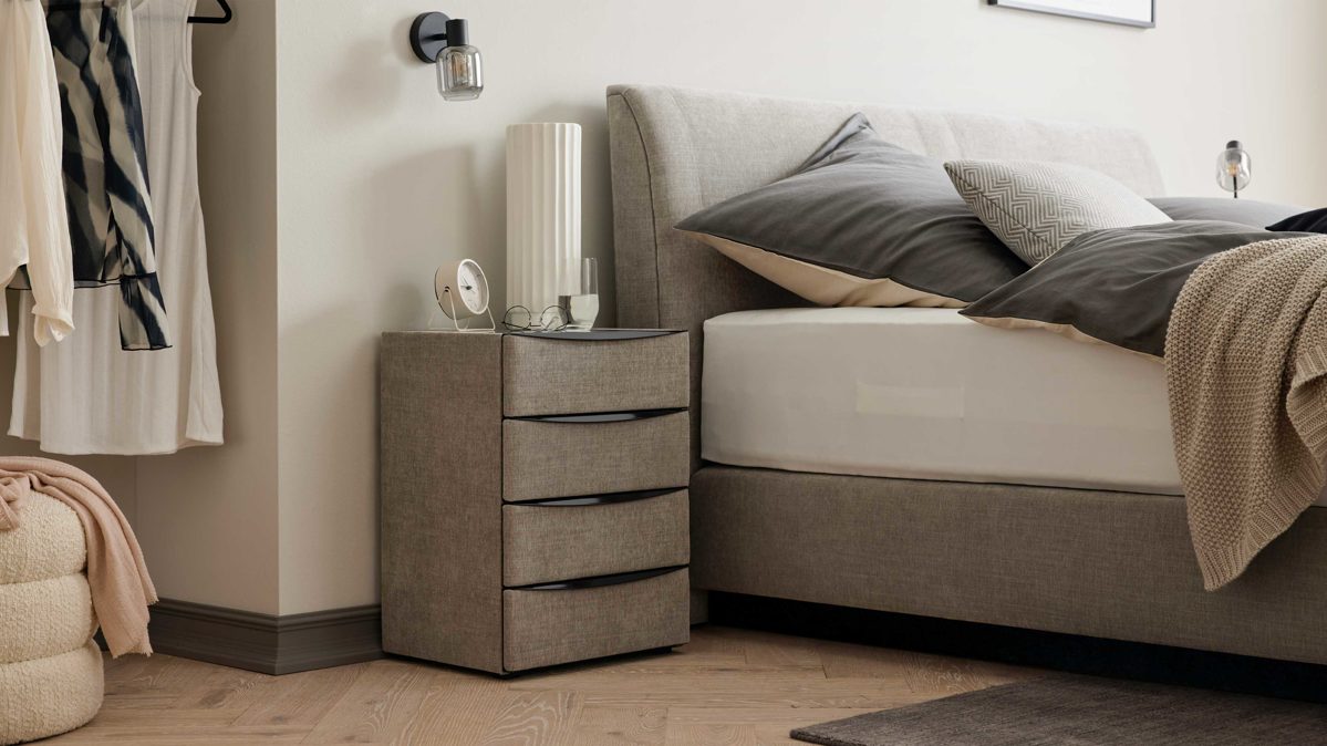 Nachtkommode Interliving aus Holz in Grau Interliving Boxspringbett Serie 1401 – Nachtkommode silberfarbener Stoffbezug Rob 533006 – vier Schubladen