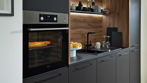 Einbauküche Interliving aus Holz in Schwarz Interliving Küche Serie 3055 mit AEG Einbaugeräten Mattschwarz & Vulkaneiche  - dreizeilig