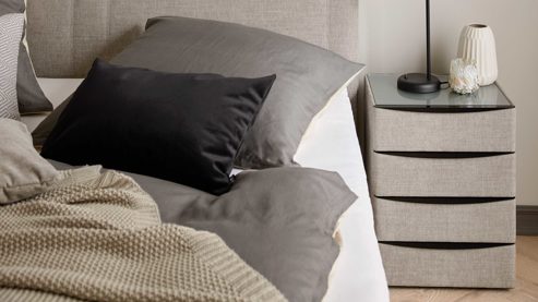 Nachtkommode Interliving aus Holz in Grau Interliving Boxspringbett Serie 1401 – Nachtkommode 64 silberfarbener Stoffbezug Rob 533006 – vier Schubladen