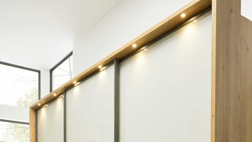 Möbelbeleuchtung Interliving aus Holz in Hellgrau Interliving Schlafzimmer Serie 1027 – Komplettzimmer 001 mit Paneelen und Licht Eiche bianco & Champagner - Liegefläche ca. 180 x 200 cm